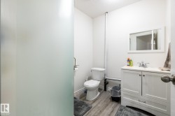 Bathroom featuring a white vanity with a white countertop, a rectangular mirror, a toilet, and wood-finish flooring - 