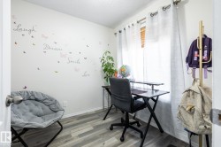 Versatile room featuring wood-finish flooring, a bright window with blinds and sheer curtains, and crisp white walls - 