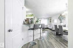 Open-concept living space featuring wood-finish flooring, a breakfast bar, and a dining area with an overhead light fixture - 