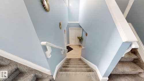 Staircase with carpeted treads and white handrails, leading down to a landing with light-toned flooring and a white paneled door - 3613 11 Street, Edmonton, AB - Indoor Photo Showing Other Room