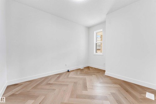 Room featuring light wood-finish flooring arranged in a herringbone pattern, white baseboards, and a single window with white trim - 4006 35 St, Beaumont, AB - Indoor Photo Showing Other Room