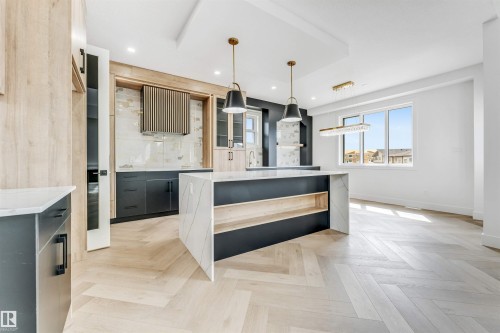 Modern kitchen featuring a waterfall island with marble-look countertop, dark cabinetry, and wood-finish flooring in a herringbone pattern - 4006 35 St, Beaumont, AB - Indoor Photo Showing Kitchen