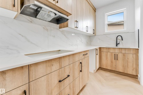 Contemporary kitchen featuring light wood-finish cabinetry with black hardware, white countertops, and a white tile backsplash - 4006 35 St, Beaumont, AB - Indoor Photo Showing Kitchen