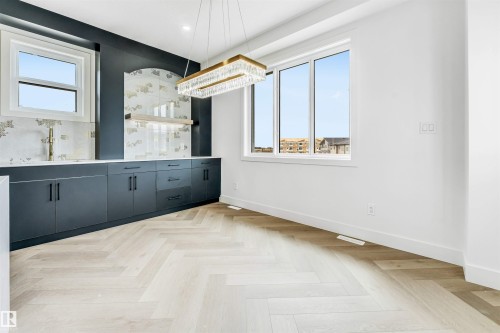 Spacious interior featuring a large window, light-toned wood-finish flooring in a herringbone pattern, and a contemporary chandelier - 4006 35 St, Beaumont, AB - Indoor
