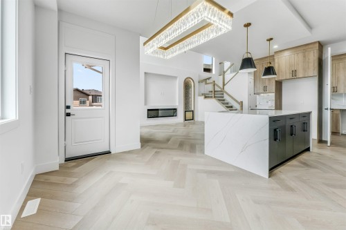 Open-concept living area featuring light wood-finish herringbone flooring, a large kitchen island with a waterfall countertop, and an integrated linear fireplace - 4006 35 St, Beaumont, AB - Indoor Photo Showing Kitchen