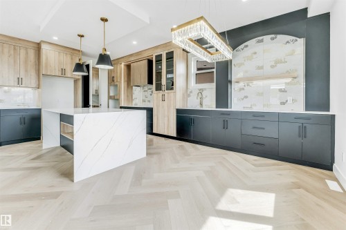 Kitchen featuring a large waterfall-edge island with integrated shelving, herringbone wood-finish flooring, a tray ceiling, and a mix of light wood-finish and dark flat-panel cabinetry - 4006 35 St, Beaumont, AB - Indoor Photo Showing Kitchen