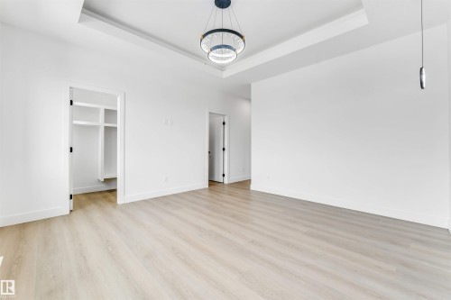 Spacious room featuring light wood-finish flooring, crisp white walls, and a recessed ceiling with a modern circular chandelier - 4006 35 St, Beaumont, AB - Indoor Photo Showing Other Room