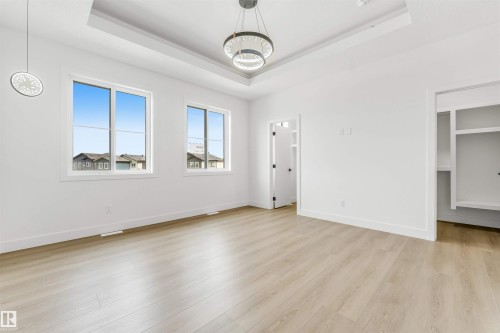 Expansive room featuring light wood-finish flooring, a tray ceiling with recessed lighting, and two contemporary pendant light fixtures - 4006 35 St, Beaumont, AB - Indoor Photo Showing Other Room