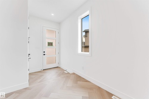 Entryway featuring light wood-finish flooring in a herringbone pattern, a contemporary door with frosted glass panels, and a tall vertical window providing natural light - 4006 35 St, Beaumont, AB - Indoor Photo Showing Other Room