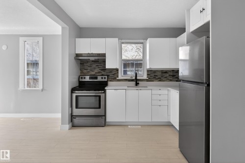 Contemporary kitchen featuring light wood-finish flooring, white cabinetry, and stainless steel appliances - 8722 112 Avenue, Edmonton, AB - Indoor Photo Showing Kitchen