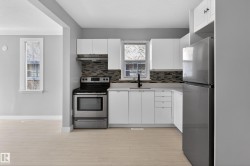 Contemporary kitchen featuring light wood-finish flooring, white cabinetry, and stainless steel appliances - 