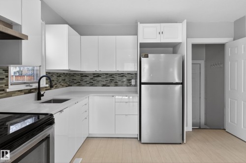 Kitchen featuring white cabinetry, light countertops, a mosaic tile backsplash, stainless steel appliances, and light wood-finish flooring - 8722 112 Avenue, Edmonton, AB - Indoor Photo Showing Kitchen With Upgraded Kitchen