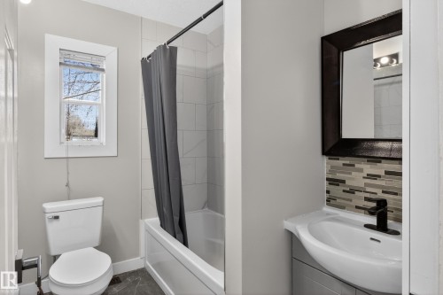 Bathroom featuring a white bathtub with tile surround, a toilet, and a vanity with an integrated sink - 8722 112 Avenue, Edmonton, AB - Indoor Photo Showing Bathroom