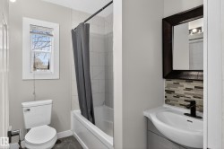 Bathroom featuring a white bathtub with tile surround, a toilet, and a vanity with an integrated sink - 