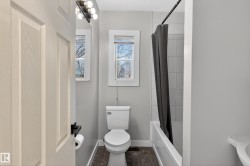 Bathroom featuring a white toilet, two windows, and a bathtub with white subway tile surround - 
