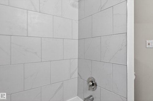 Shower enclosure with large format white tile, subtle veining, chrome fixtures, and a white tub surround - 8722 112 Avenue, Edmonton, AB - Indoor