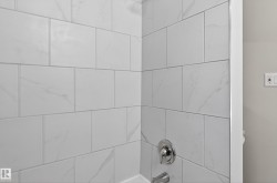 Shower enclosure with large format white tile, subtle veining, chrome fixtures, and a white tub surround - 