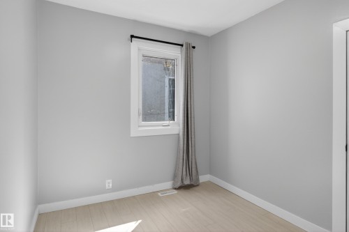 Bright room featuring a window with a curtain rod, light wood-finish flooring, white baseboards, and light gray painted walls - 8722 112 Avenue, Edmonton, AB - Indoor Photo Showing Other Room