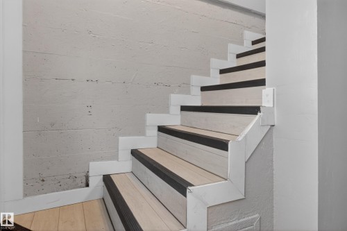 Staircase featuring wood-finish treads with dark anti-slip strips, white risers, and a textured concrete wall - 8722 112 Avenue, Edmonton, AB - Indoor Photo Showing Other Room