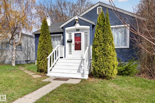 Stucco exterior featuring a prominent red entry door with sidelights, white porch stairs, and a gabled roofline - 8722 112 Avenue, Edmonton, AB - Outdoor