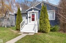 Stucco exterior featuring a prominent red entry door with sidelights, white porch stairs, and a gabled roofline - 8722 112 Avenue, Edmonton, AB  - Outdoor 