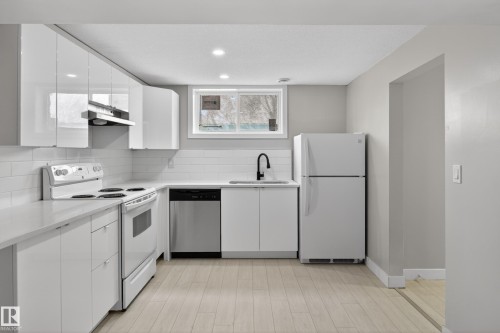 Modern kitchen featuring white glossy cabinetry, light wood-finish flooring, white subway tile backsplash, stainless steel dishwasher, and a black gooseneck faucet - 8722 112 Avenue, Edmonton, AB - Indoor Photo Showing Kitchen