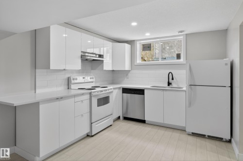 Modern kitchen featuring white cabinetry, light countertops, subway tile backsplash, and wood-finish flooring - 8722 112 Avenue, Edmonton, AB - Indoor Photo Showing Kitchen