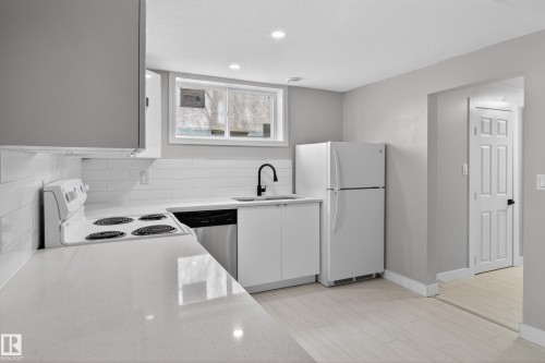 Modern kitchen featuring white cabinetry, light-toned countertops, a full suite of appliances, subway tile backsplash, and recessed lighting - 8722 112 Avenue, Edmonton, AB - Indoor Photo Showing Kitchen