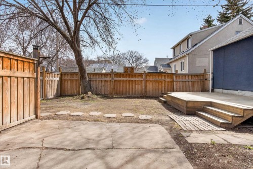 Expansive backyard featuring a large wooden deck with multiple steps, a full perimeter privacy fence, a concrete patio area, and mature trees - 8722 112 Avenue, Edmonton, AB - Outdoor