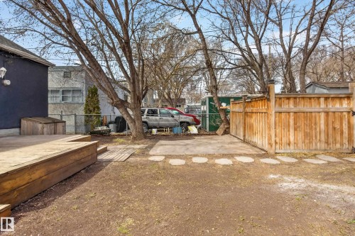 Expansive backyard with a wooden deck, natural wood privacy fence, concrete pad, and stone paver pathway - 8722 112 Avenue, Edmonton, AB - Outdoor