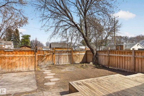 Expansive fenced backyard featuring a wood deck, concrete patio, stepping stone pathway, and mature tree - 8722 112 Avenue, Edmonton, AB - Outdoor