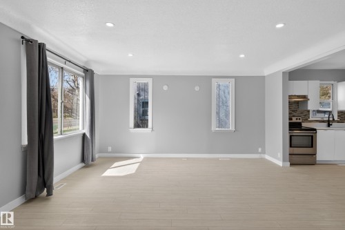 Bright living area featuring light wood-finish flooring, recessed lighting, and a wide window with dark drapery - 8722 112 Avenue, Edmonton, AB - Indoor
