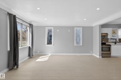Bright living area featuring light wood-finish flooring, recessed lighting, and a wide window with dark drapery - 