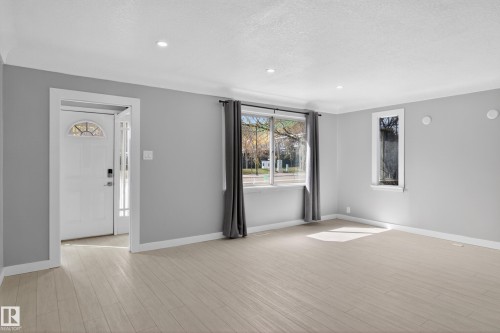 Spacious room featuring light wood-finish flooring, recessed lighting, and a white entry door with a decorative transom - 8722 112 Avenue, Edmonton, AB - Indoor Photo Showing Other Room