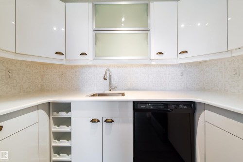 Kitchen featuring white cabinetry, solid surface countertops, a mosaic tile backsplash, stainless steel sink with gooseneck faucet, and integrated wine storage - 302 9138 83 Avenue, Edmonton, AB - Indoor Photo Showing Kitchen