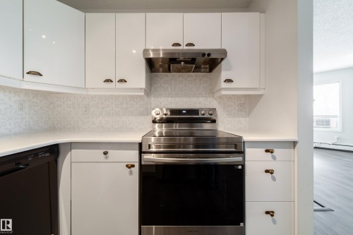 Contemporary kitchen featuring white cabinetry, a patterned backsplash, stainless steel range, matching range hood, and light-toned countertops - 302 9138 83 Avenue, Edmonton, AB - Indoor Photo Showing Kitchen