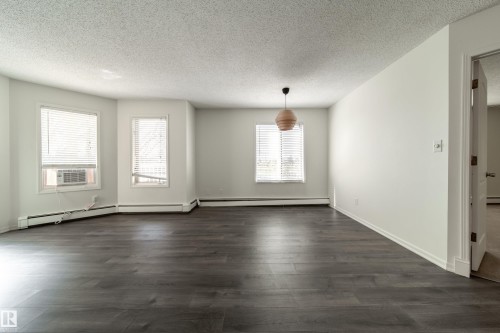 Expansive room featuring dark wood-finish flooring, white walls, and a textured white ceiling - 302 9138 83 Avenue, Edmonton, AB - Indoor Photo Showing Other Room
