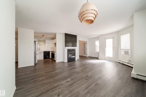 Open-concept living area featuring wood-finish flooring, a modern fireplace with a dark tile surround, and a contemporary pendant light fixture - 302 9138 83 Avenue, Edmonton, AB - Indoor Photo Showing Other Room With Fireplace
