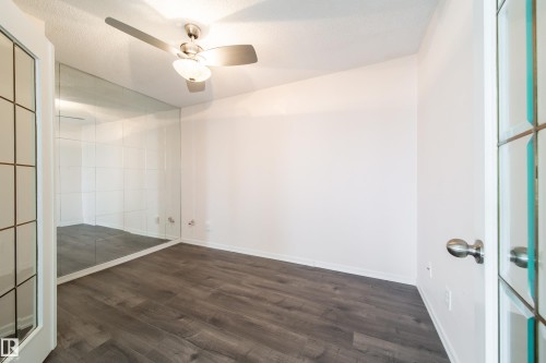Room featuring wood-finish flooring, a full-wall mirror, and a ceiling fan with integrated lighting - 302 9138 83 Avenue, Edmonton, AB - Indoor Photo Showing Other Room