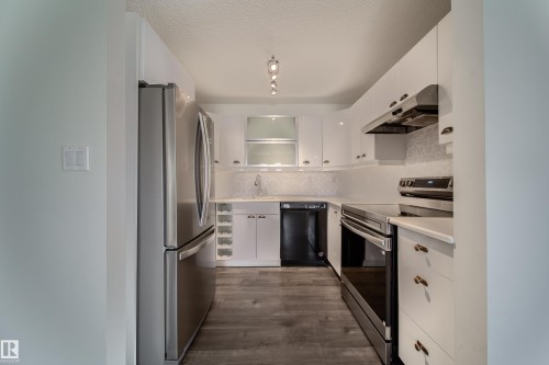 Galley kitchen featuring stainless steel appliances, white cabinetry with contemporary hardware, light countertops, and wood-finish flooring - 302 9138 83 Avenue, Edmonton, AB - Indoor Photo Showing Kitchen