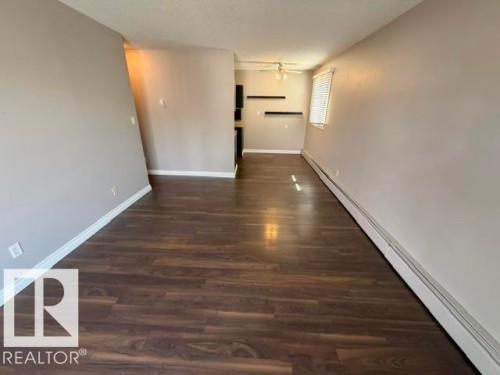 Spacious room featuring wood-finish flooring, light gray wall paint, and white baseboards - 201 11324 97 Street Nw, Edmonton, AB - Indoor Photo Showing Other Room