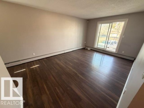 Spacious room featuring wood-finish flooring, light neutral wall tones, and a large sliding glass door - 201 11324 97 Street Nw, Edmonton, AB - Indoor Photo Showing Other Room