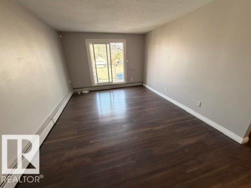 Living area featuring wood-finish flooring, light grey painted walls, white baseboards, and a sliding glass door - 201 11324 97 Street Nw, Edmonton, AB - Indoor Photo Showing Other Room