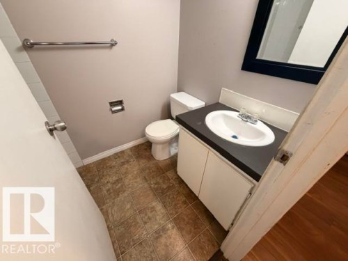 Compact bathroom featuring a white vanity with a dark countertop, an oval undermount sink, and a framed mirror - 201 11324 97 Street Nw, Edmonton, AB - Indoor Photo Showing Bathroom