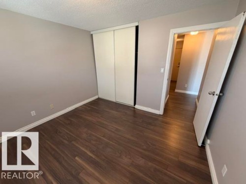 Room featuring wood-finish flooring, a neutral wall palette, white baseboards, and a closet with sliding panel doors - 201 11324 97 Street Nw, Edmonton, AB - Indoor Photo Showing Other Room