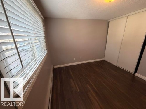 Room featuring wood-finish flooring, neutral wall paint, white baseboards, and a window with horizontal blinds - 201 11324 97 Street Nw, Edmonton, AB - Indoor Photo Showing Other Room