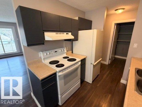 Kitchen featuring dark cabinetry, neutral countertops, a white electric range, and a white refrigerator - 201 11324 97 Street Nw, Edmonton, AB - Indoor Photo Showing Kitchen