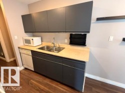 Kitchenette featuring dark gray cabinetry, a light-toned countertop, and a double basin stainless steel sink - 