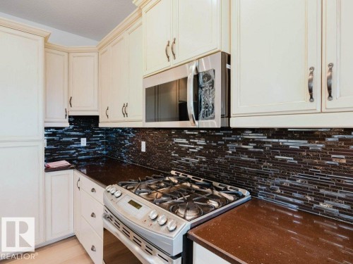 White cabinetry with crown molding, stainless steel microwave, gas range, dark brown countertops, and a mosaic tile backsplash - 15867 11 Avenue, Edmonton, AB - Indoor Photo Showing Kitchen