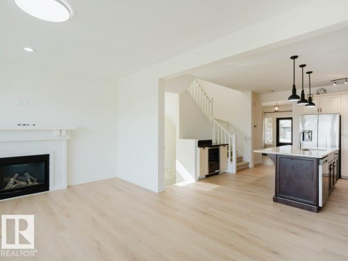 Spacious living area featuring light wood-finish flooring and a white mantel over an electric fireplace - 15867 11 Avenue, Edmonton, AB - Indoor Photo Showing Living Room With Fireplace